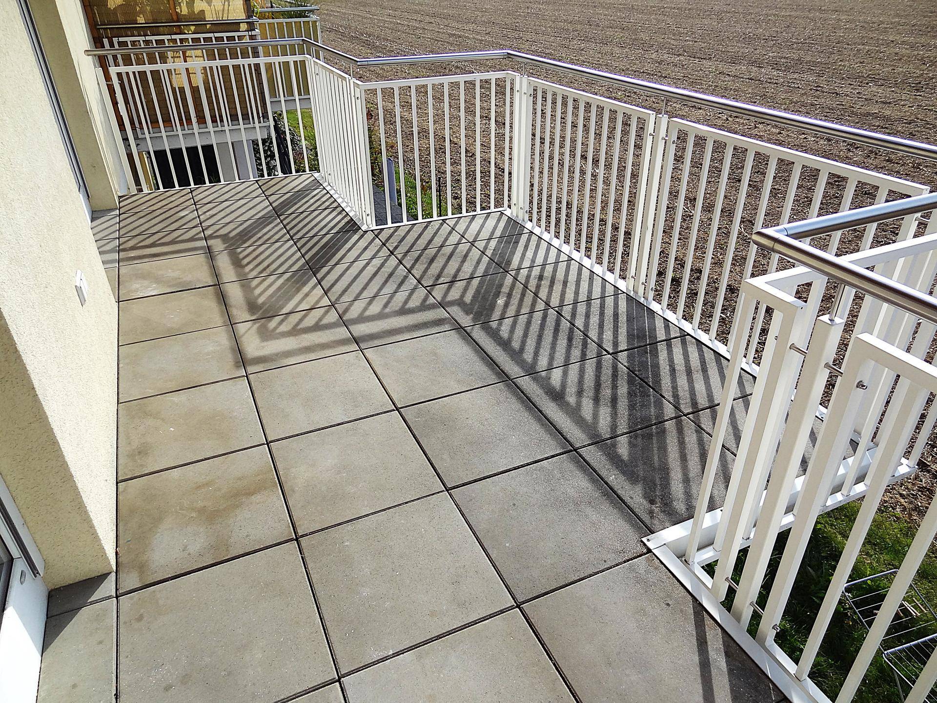 Großer Balkon mit grauen Fliesen und Blick auf die umliegende Landschaft und Felder.
