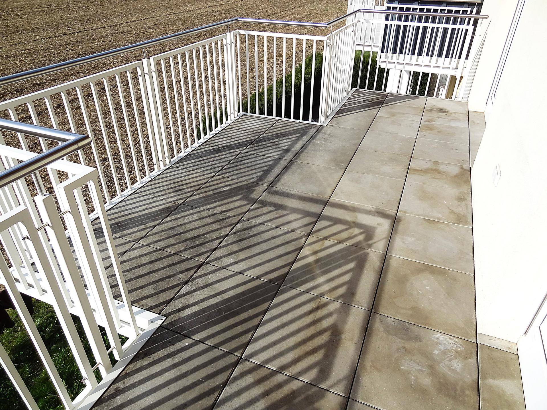 Geräumiger Balkon mit grauen Bodenfliesen und weißem Metallgeländer, bietet Platz zum Entspannen.
