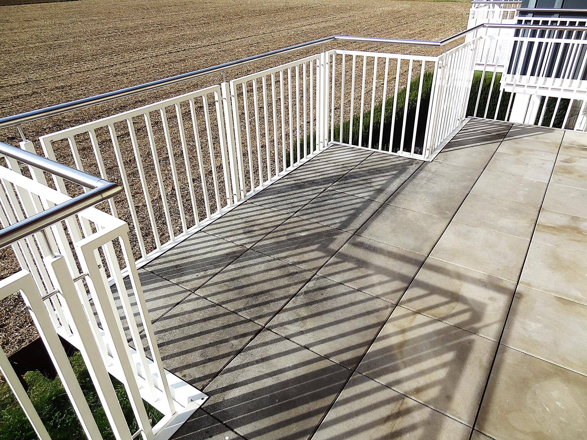 Sonniger Balkon mit grauen Fliesen und weitem Blick über Felder und grüne Hügel.