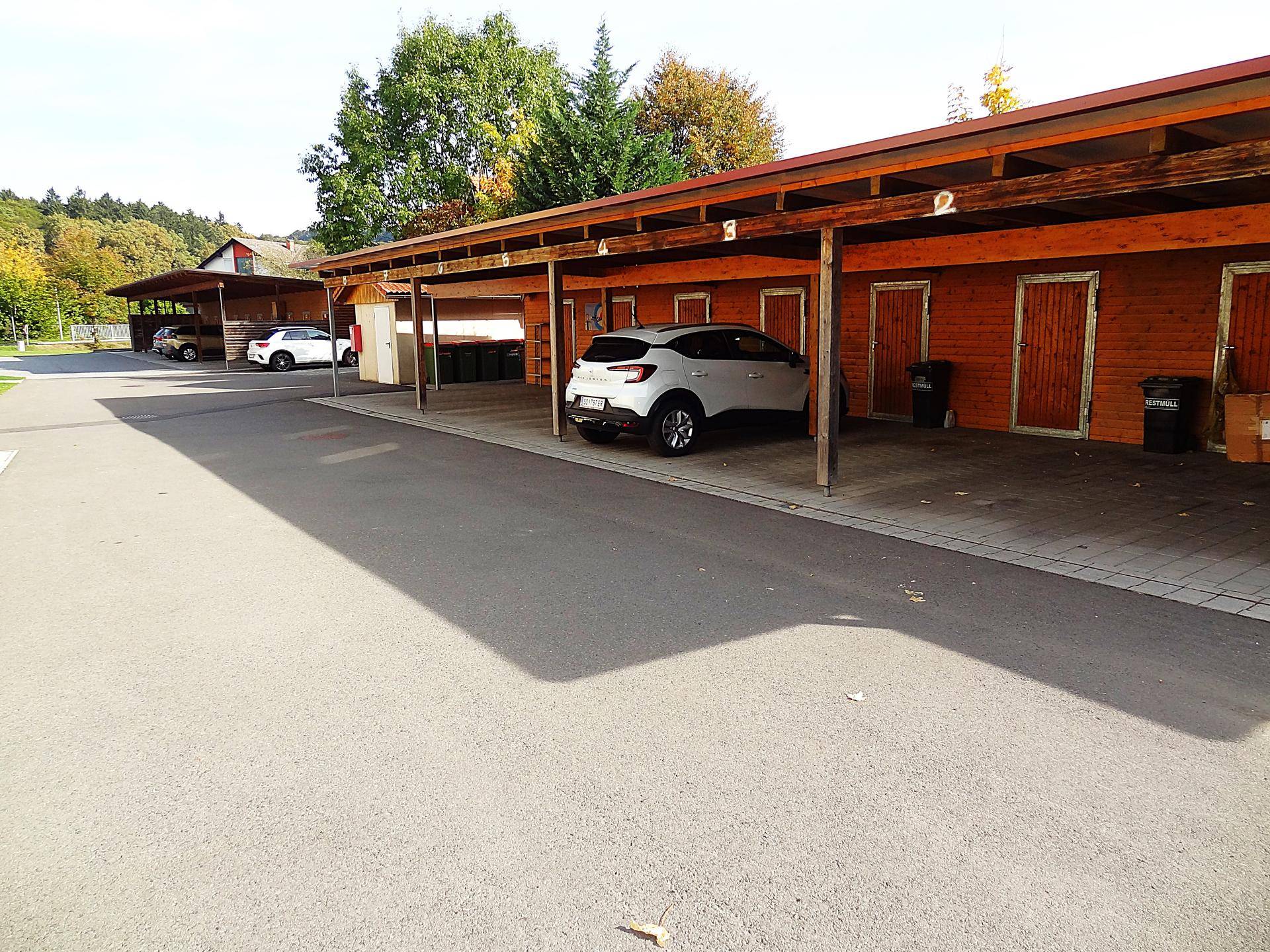 Mehrere Carports mit Holzkonstruktion und angrenzenden Abstellräumen, eingebettet in die Natur.