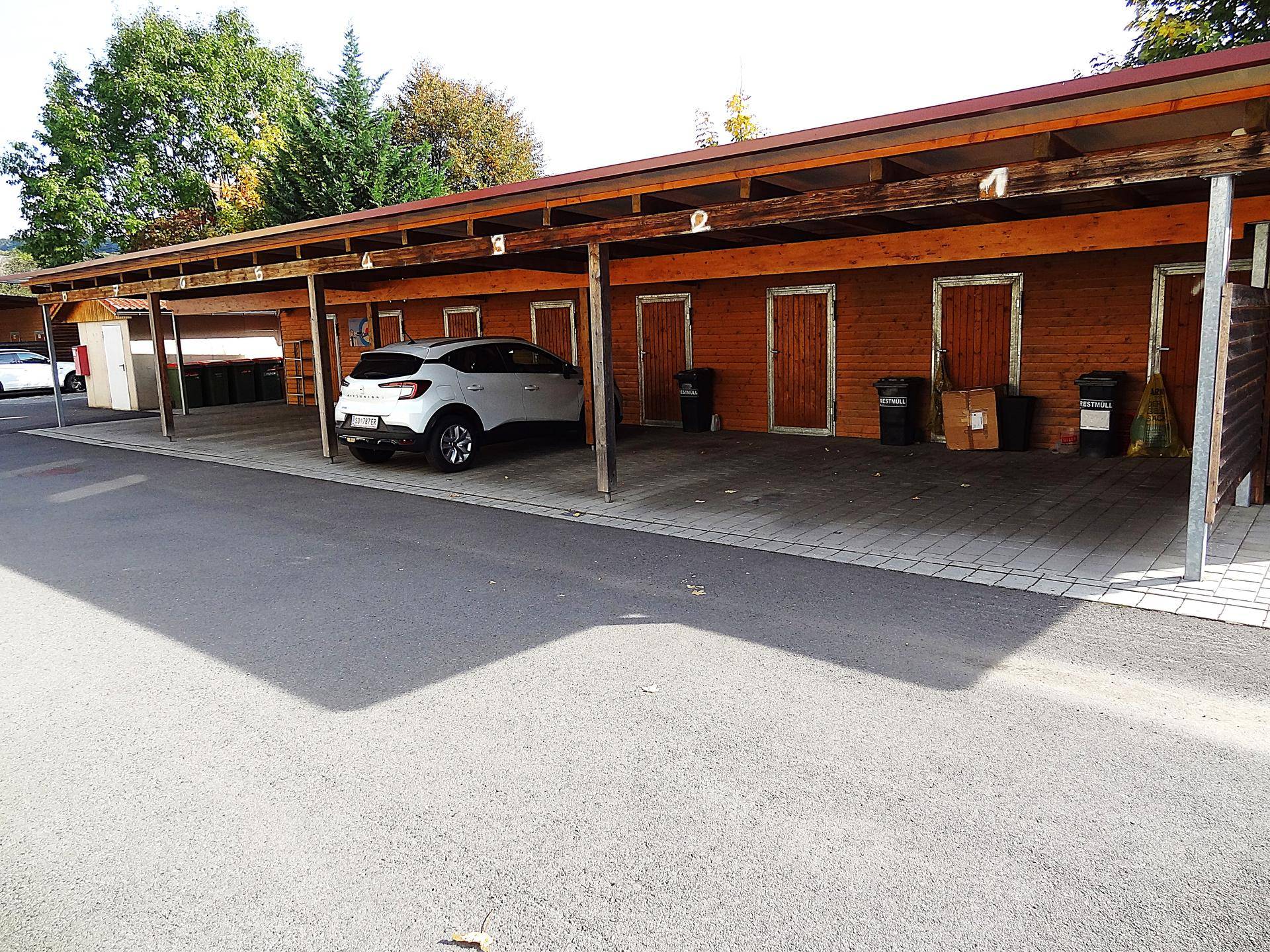 Langer Carport mit Holzüberdachung und mehreren Abstellkammern, bietet geschützten Parkraum.