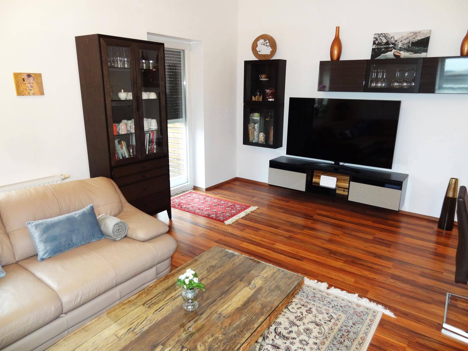 Wohnbereich mit Ledersofa, Medienschrank und Zugang zum Balkon.