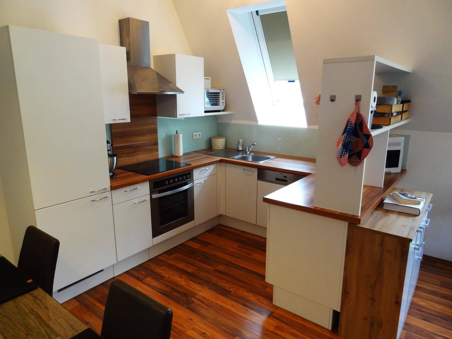 Moderne Einbauküche mit weißen Schränken, Holzarbeitsplatten und Dachfenster.