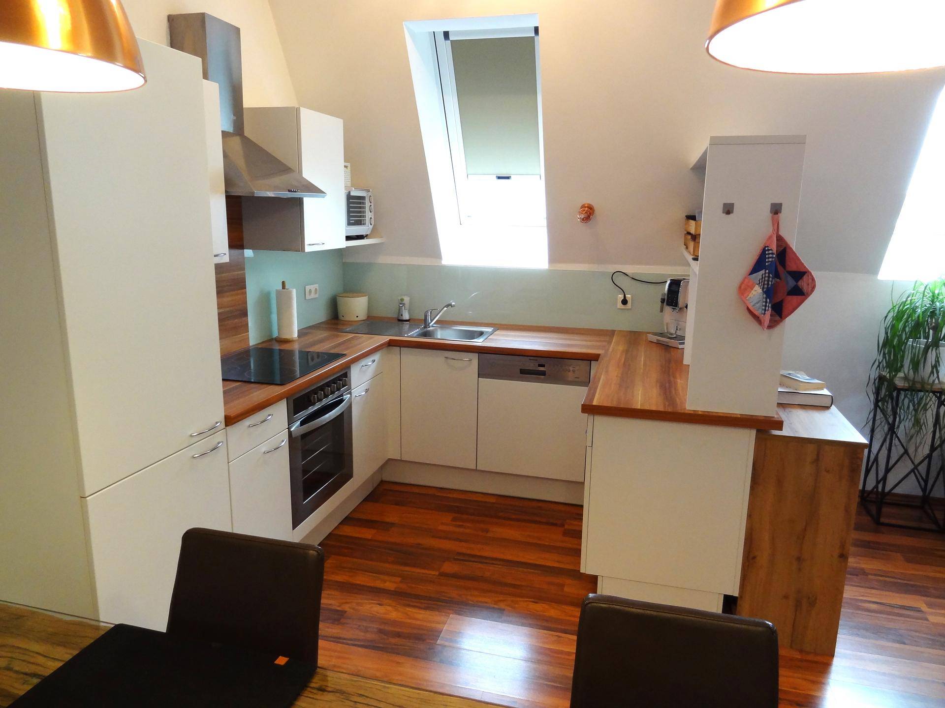 Moderne Einbauküche mit weißen Schränken, Holzarbeitsplatten und Dachfenster.