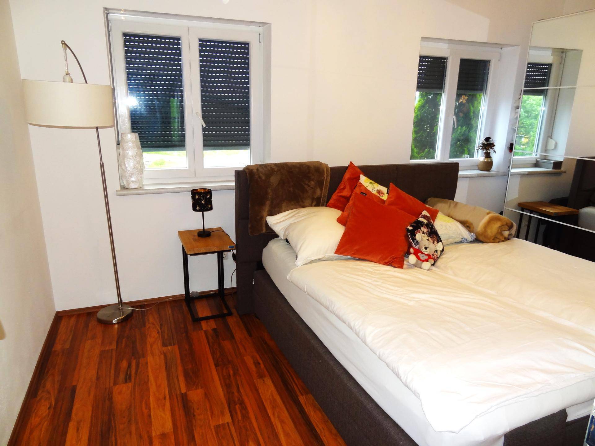 Helles Schlafzimmer mit Doppelbett, Holzboden und Stehlampe.