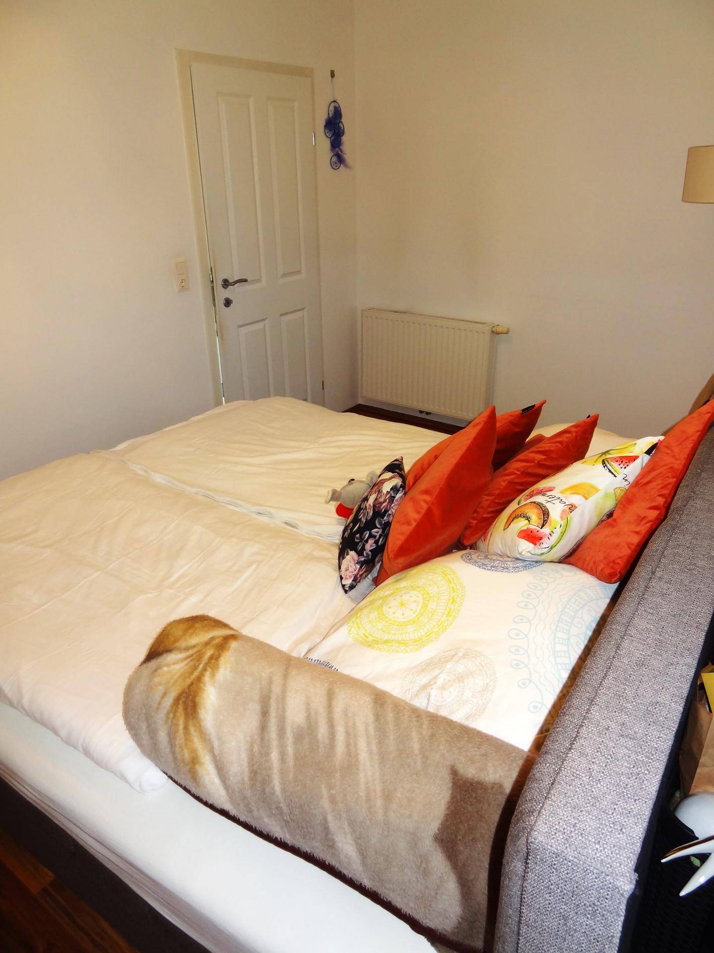 Helles Schlafzimmer mit Doppelbett, Holzboden und Heizkörper.