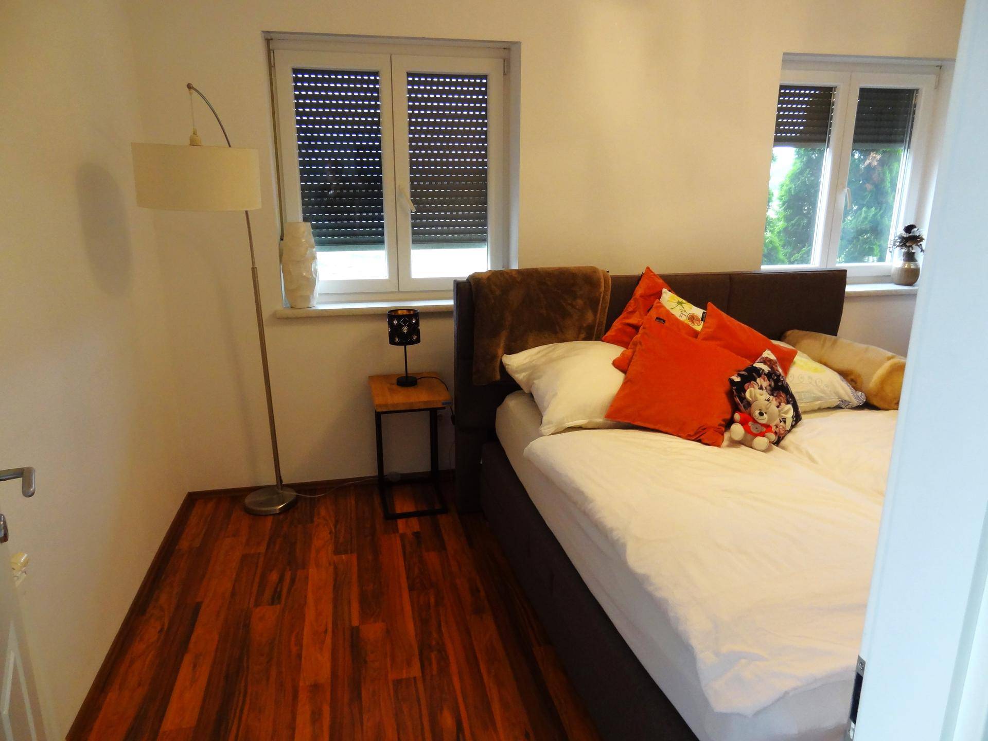 Schlafzimmer mit Doppelbett, Holzboden und Fenster mit Rollläden.