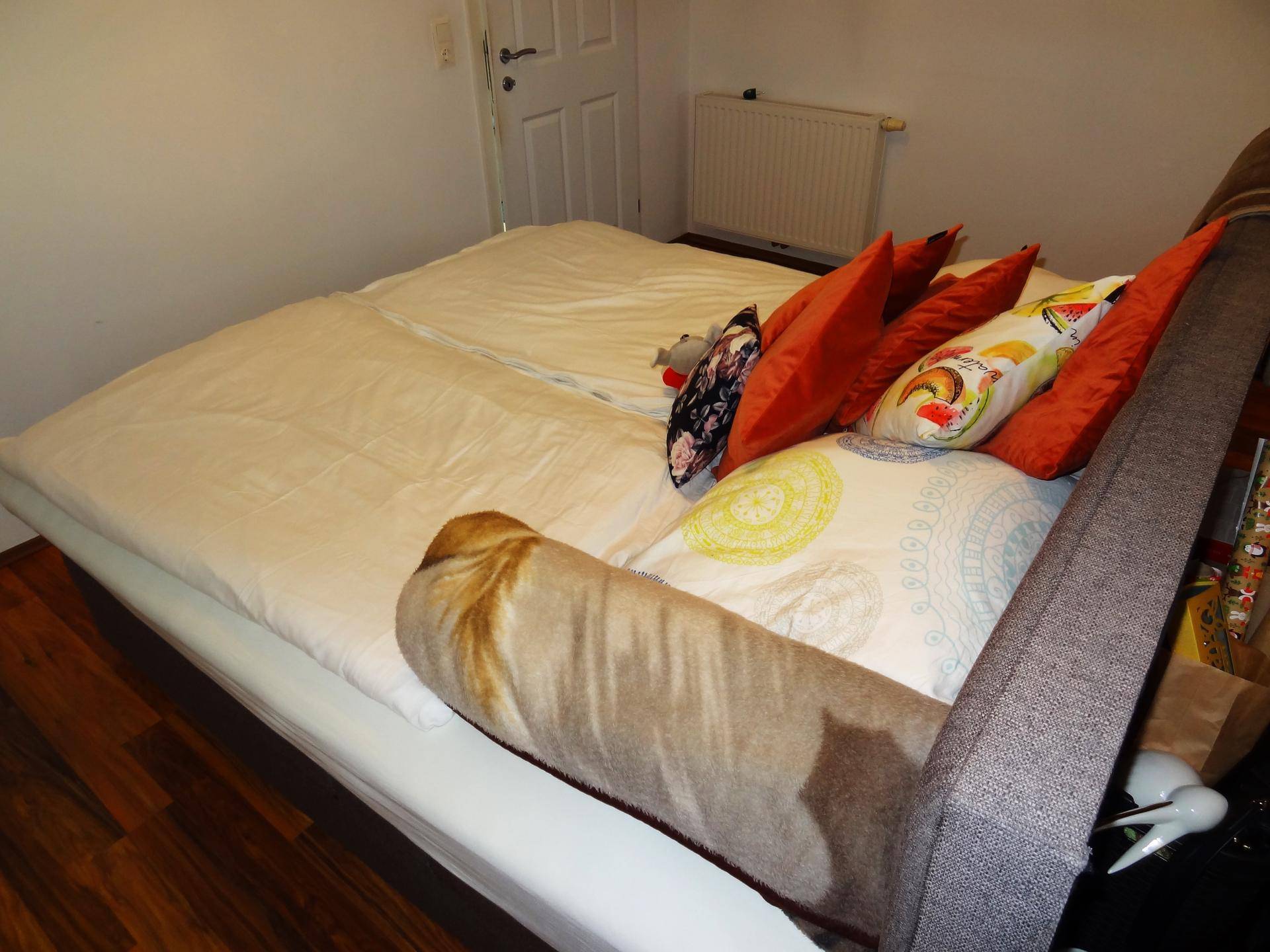Schlafzimmer mit Doppelbett, Holzboden und farbigen Kissen.