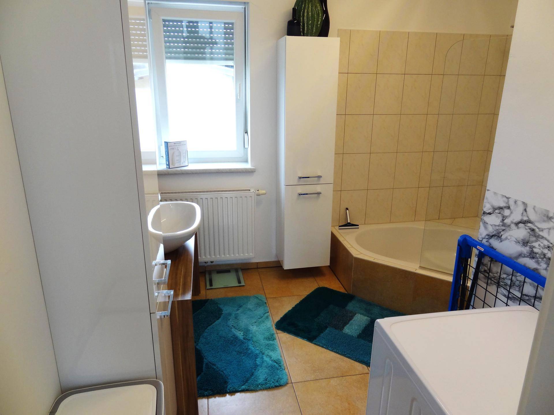 Funktionales Badezimmer mit Eckbadewanne, Duschfunktion, Waschbecken und Fenster für Tageslicht.
