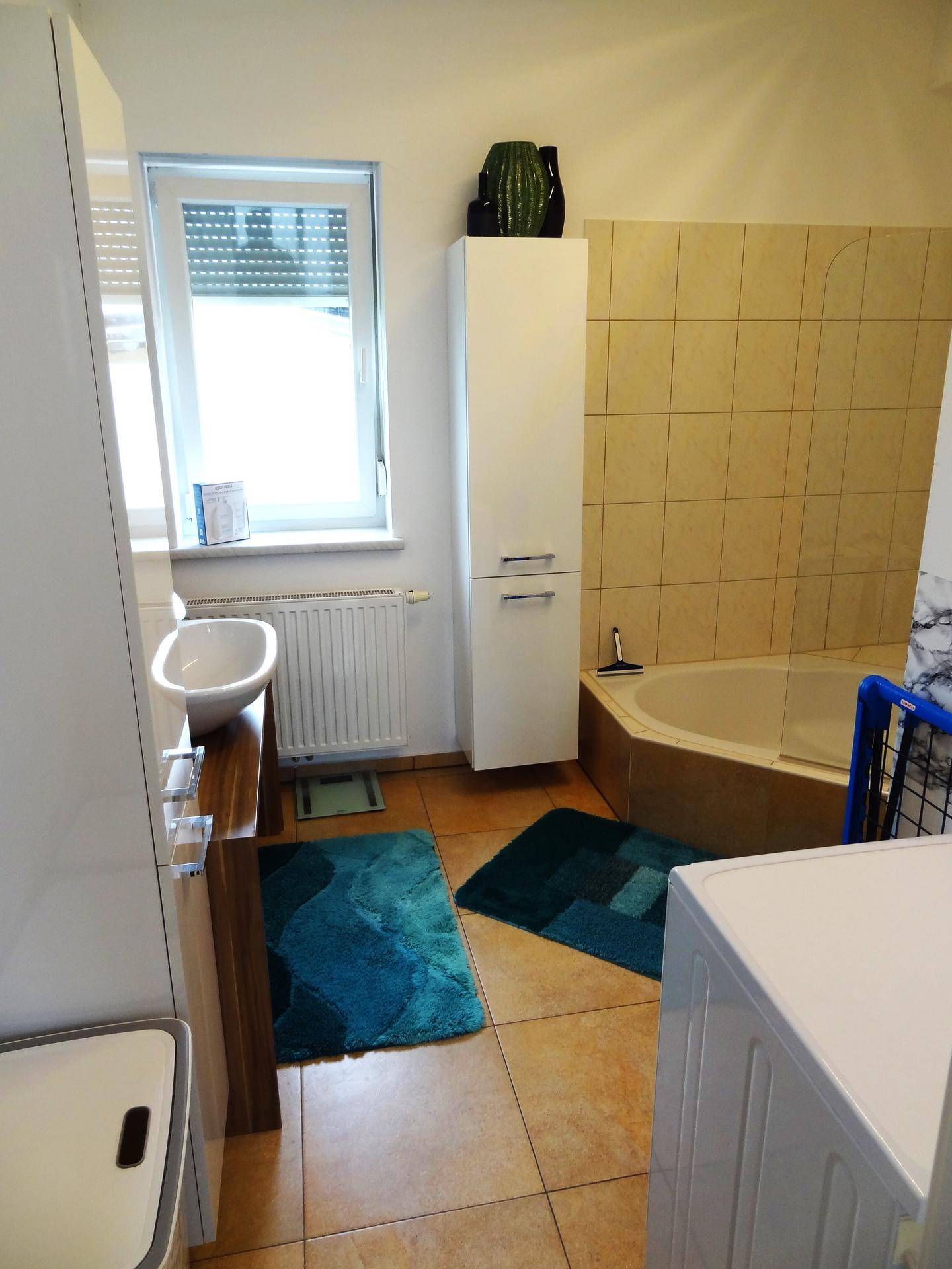 Helles Badezimmer mit Fliesenboden, Eckbadewanne und einem Fenster, das für gute Belüftung sorgt.