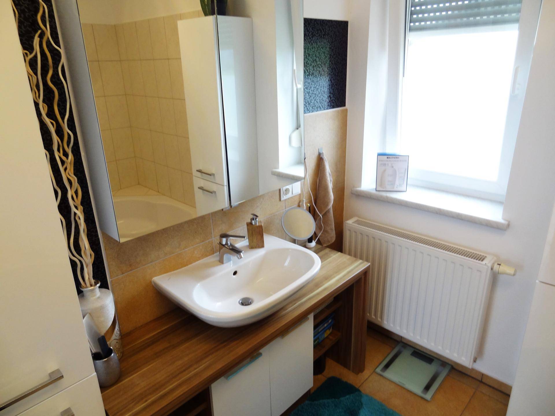 Heller Waschbereich im Badezimmer mit modernem Waschbecken, Holzablage und großem Spiegelschrank.