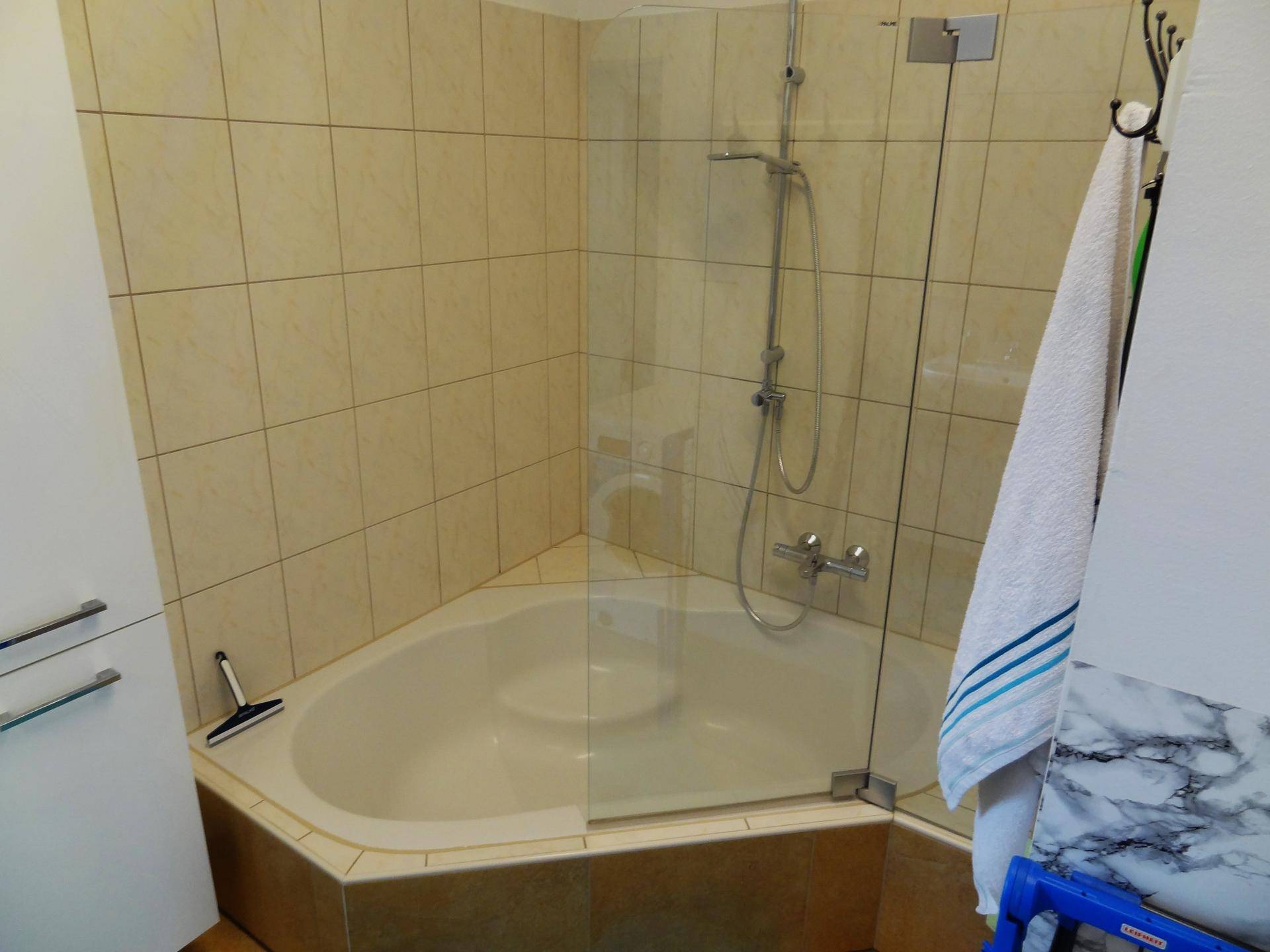 Badezimmer mit Eckbadewanne, Duscharmatur und praktischer Glasduschwand für Spritzschutz.