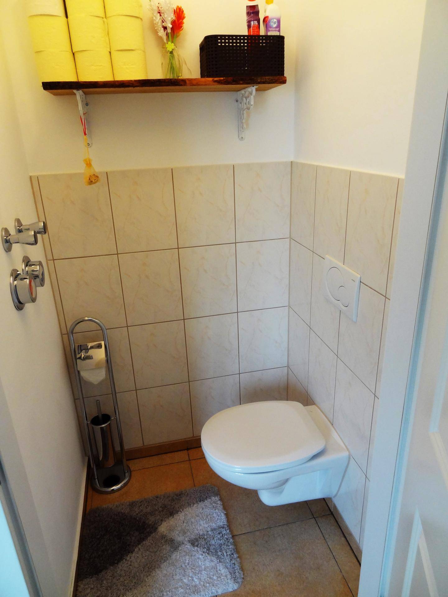 Gäste-WC mit wandhängender Toilette und halbhoch gefliesten Wänden in neutralen Farbtönen.