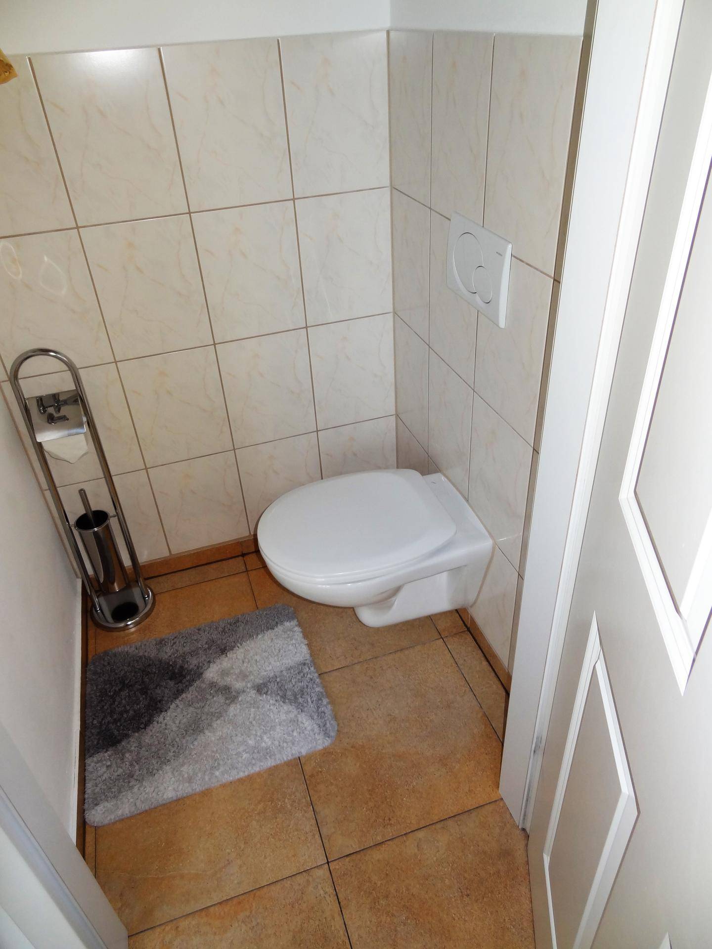 Funktionales Gäste-WC mit Fliesenboden und wandmontierter Toilette, platzsparend und modern.