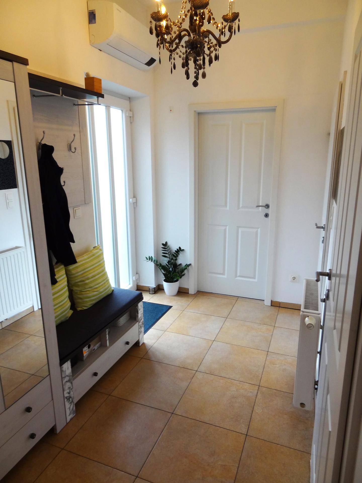 Heller Eingangsbereich mit Fliesenboden, Garderobe und einem eleganten Kronleuchter als Blickfang.