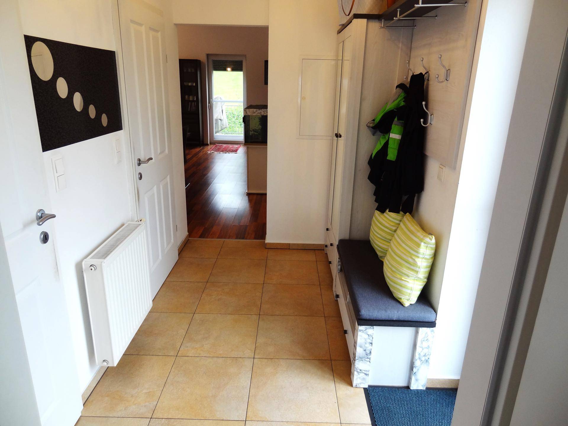 Heller Flur mit Garderobe, Fliesenboden und nahtlosem Übergang zu einem Parkettboden.