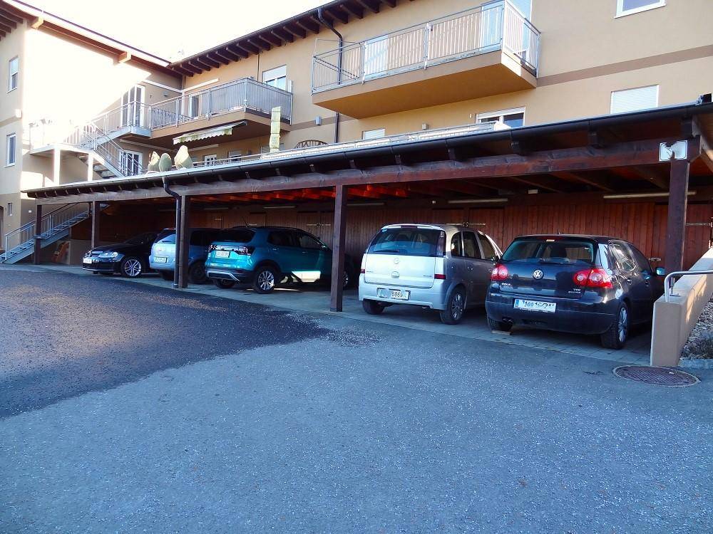 Überdachter Carport-Bereich mit mehreren geparkten Fahrzeugen und angrenzendem Wohngebäude.