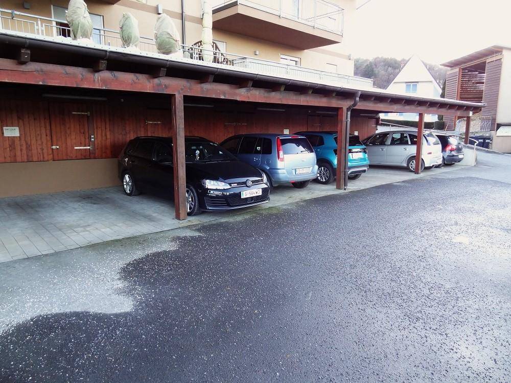 Reihe von überdachten Parkplätzen unter einem Holzcarport neben einem Wohngebäude.