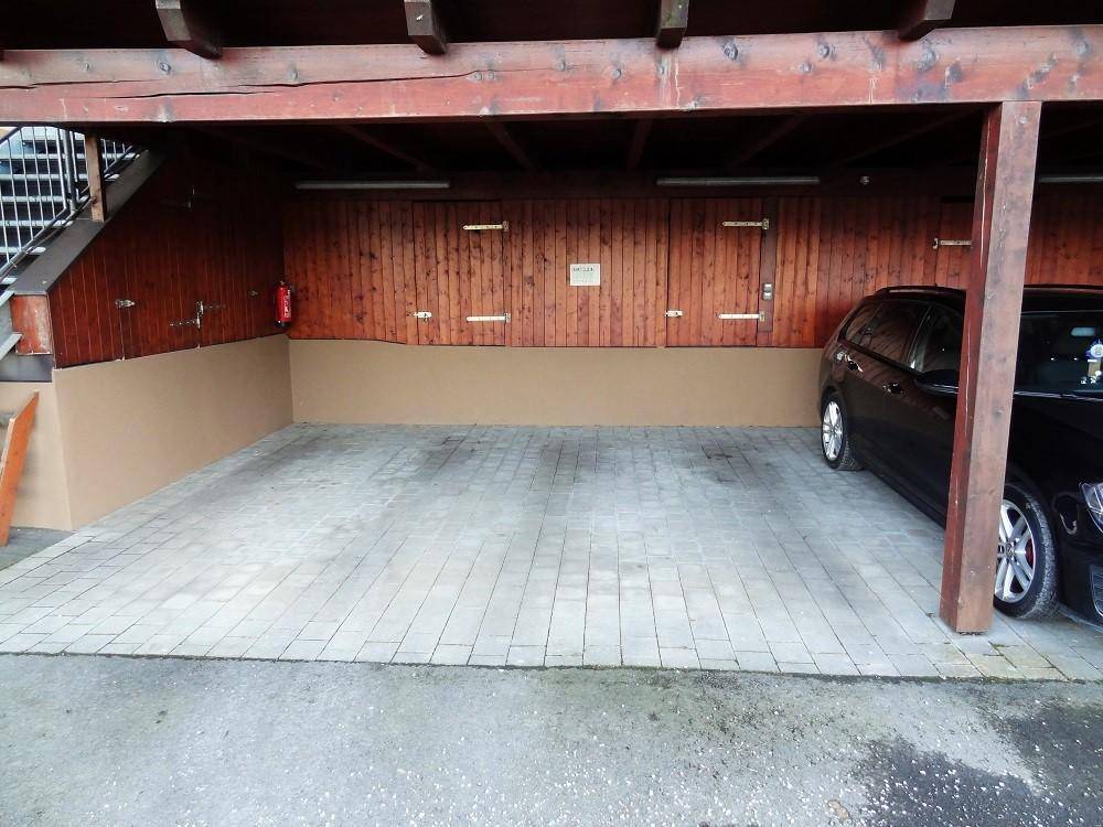 Leerer Carport-Stellplatz mit gepflastertem Boden und Holzwänden, bereit zur Nutzung.