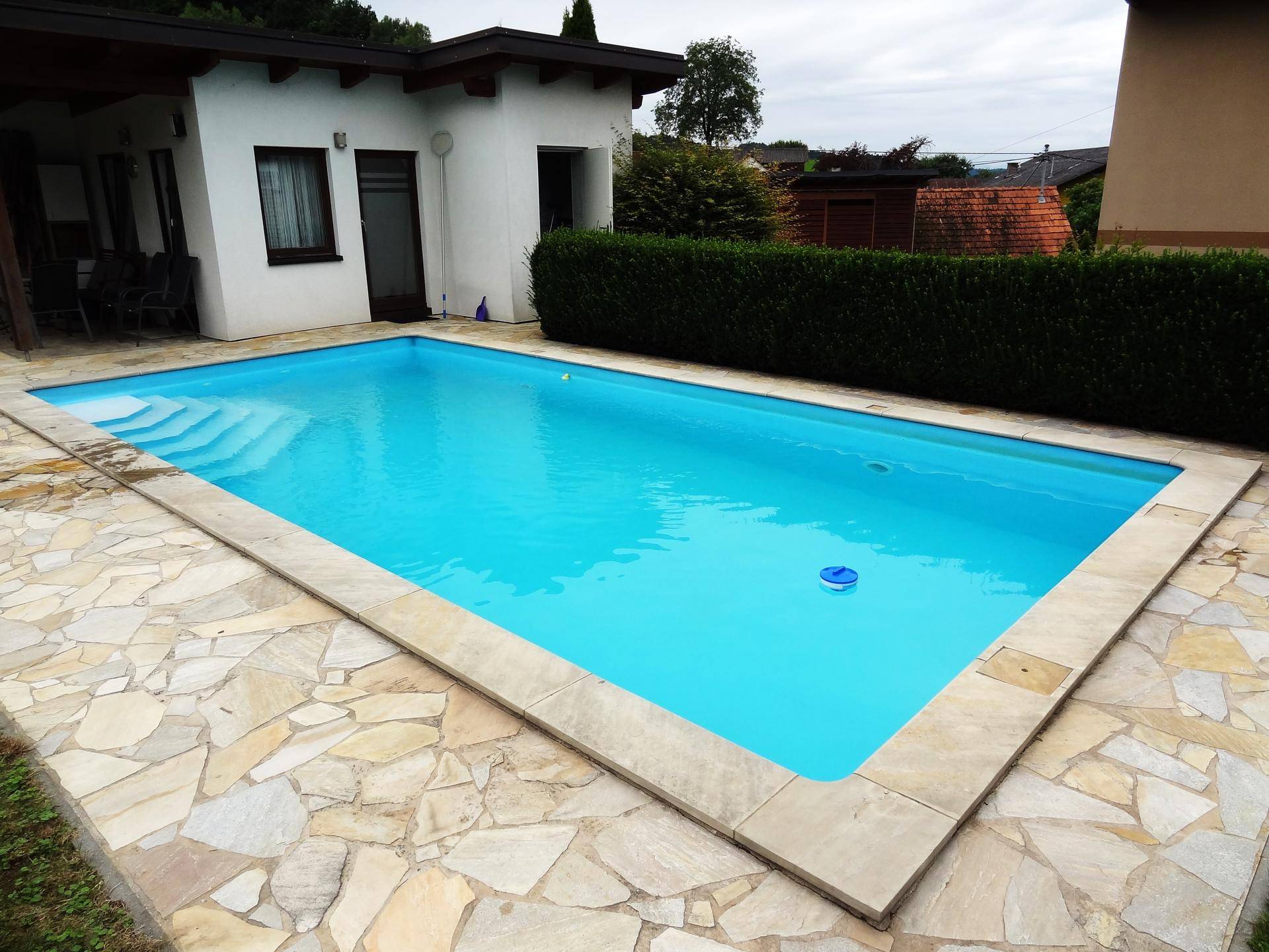 Großer, sauberer Swimmingpool mit Steinfliesenumrandung in einem gepflegten Gartenbereich.