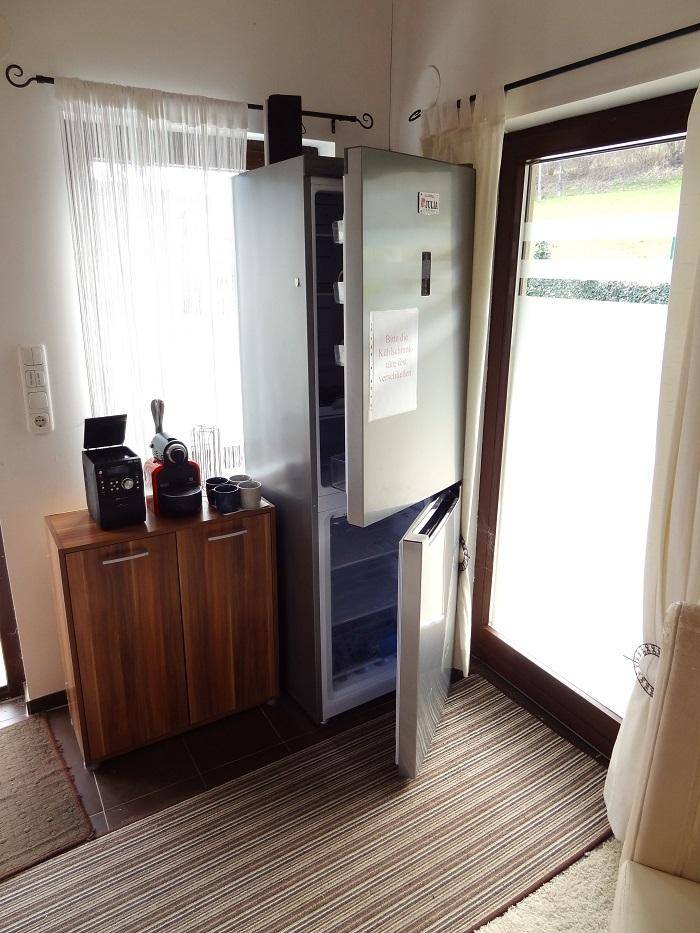 Ecke mit Kühlschrank, Kaffeemaschine und Holzschrank neben einem Fenster.