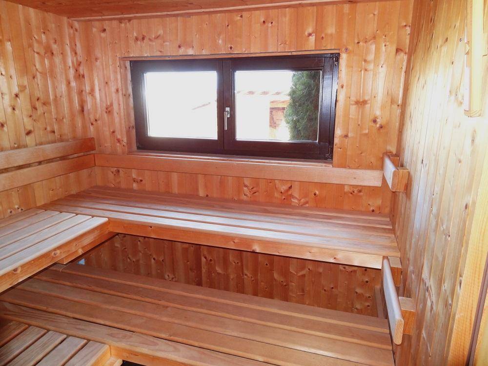 Helle Holzsauna mit breiten Sitzbänken und einem Fenster, das Tageslicht hereinlässt.
