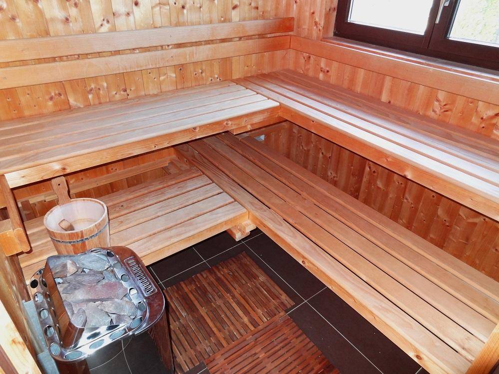Traditionelle Holzsauna mit Saunaofen, Holzbänken und einem Eimer für Aufgüsse.