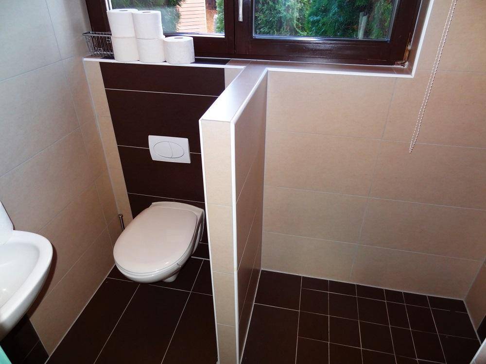 Zeitgemäßes Badezimmer mit WC, Waschbecken und Duschbereich, hell gefliest und mit Fenster.