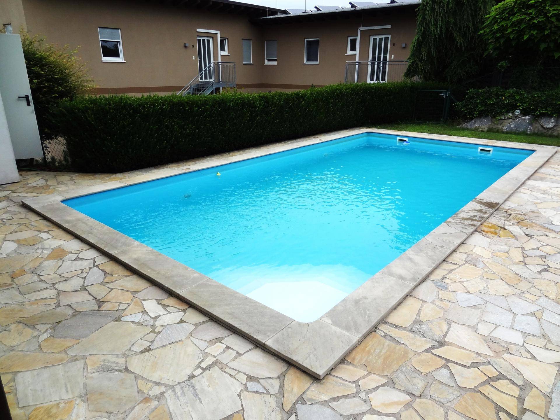 Gepflegter Swimmingpool im Garten mit Natursteinumrandung und Blick auf das Wohngebäude.