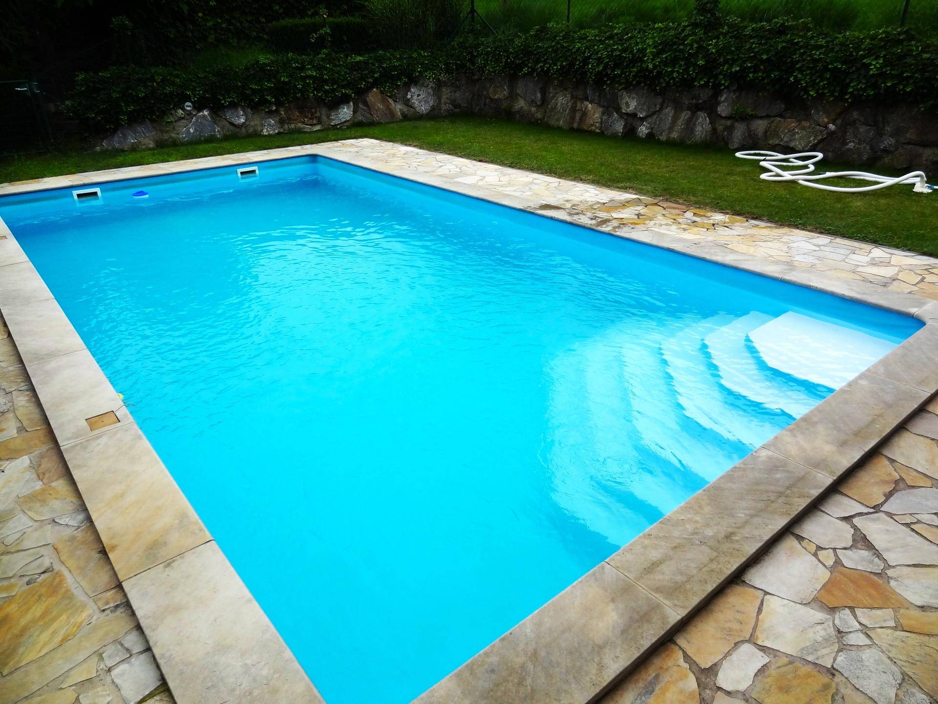 Nahaufnahme eines Swimmingpools mit klarem Wasser und breiten Einstiegsstufen im Garten.