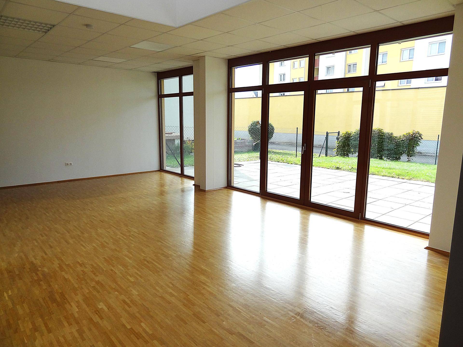 Heller Raum mit Parkettboden und großen Fenstern, die einen Blick auf den Garten und die Umgebung bieten.