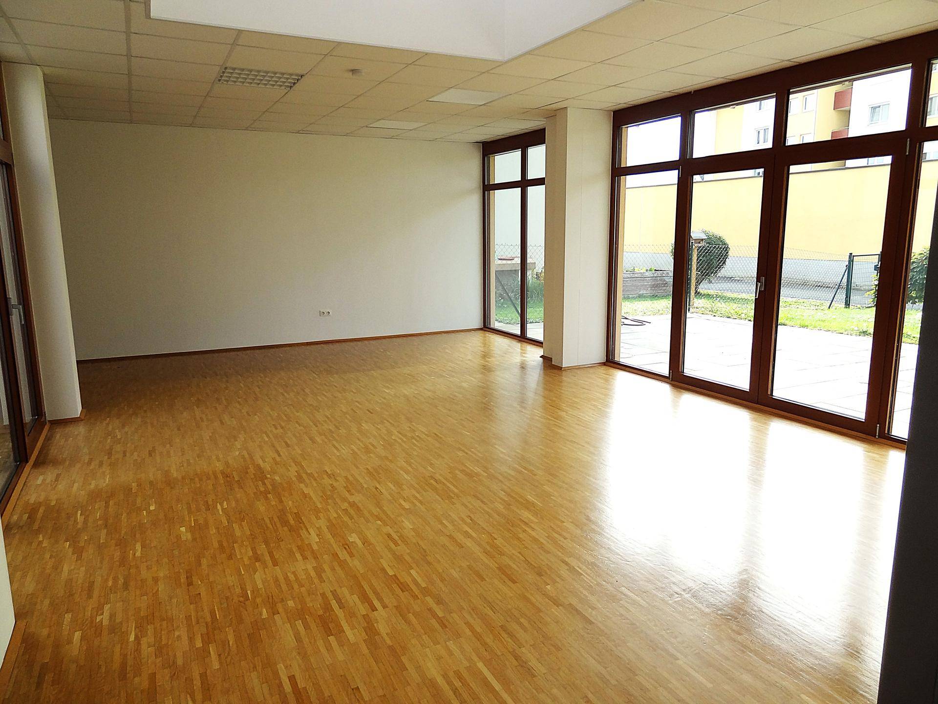 Großer, heller Raum mit Parkettboden und vielen Fenstern, die viel Tageslicht hereinlassen.
