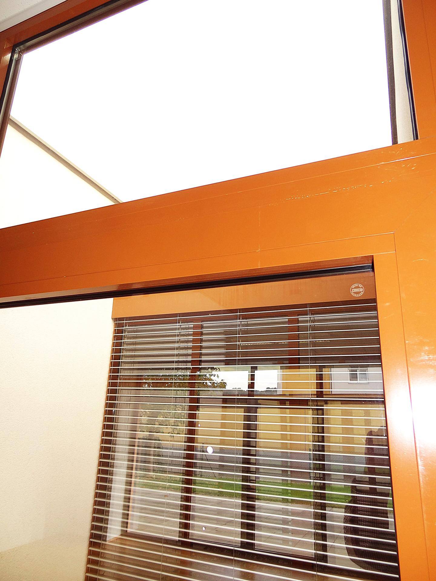 Detailansicht eines modernen Fensters mit braunem Rahmen und integrierten Jalousien.