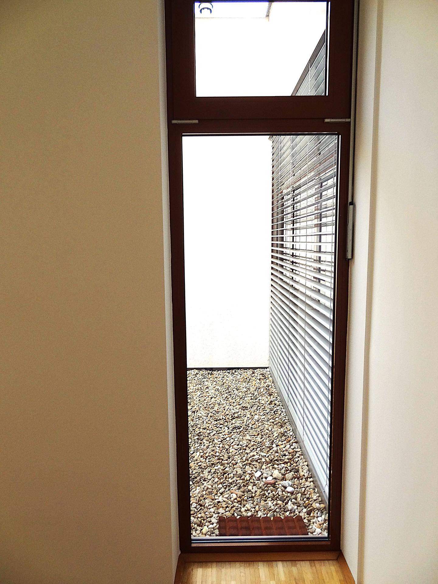 Hohes Fenster mit Blick auf einen kleinen Kieshof, das viel Tageslicht in den Raum lässt.