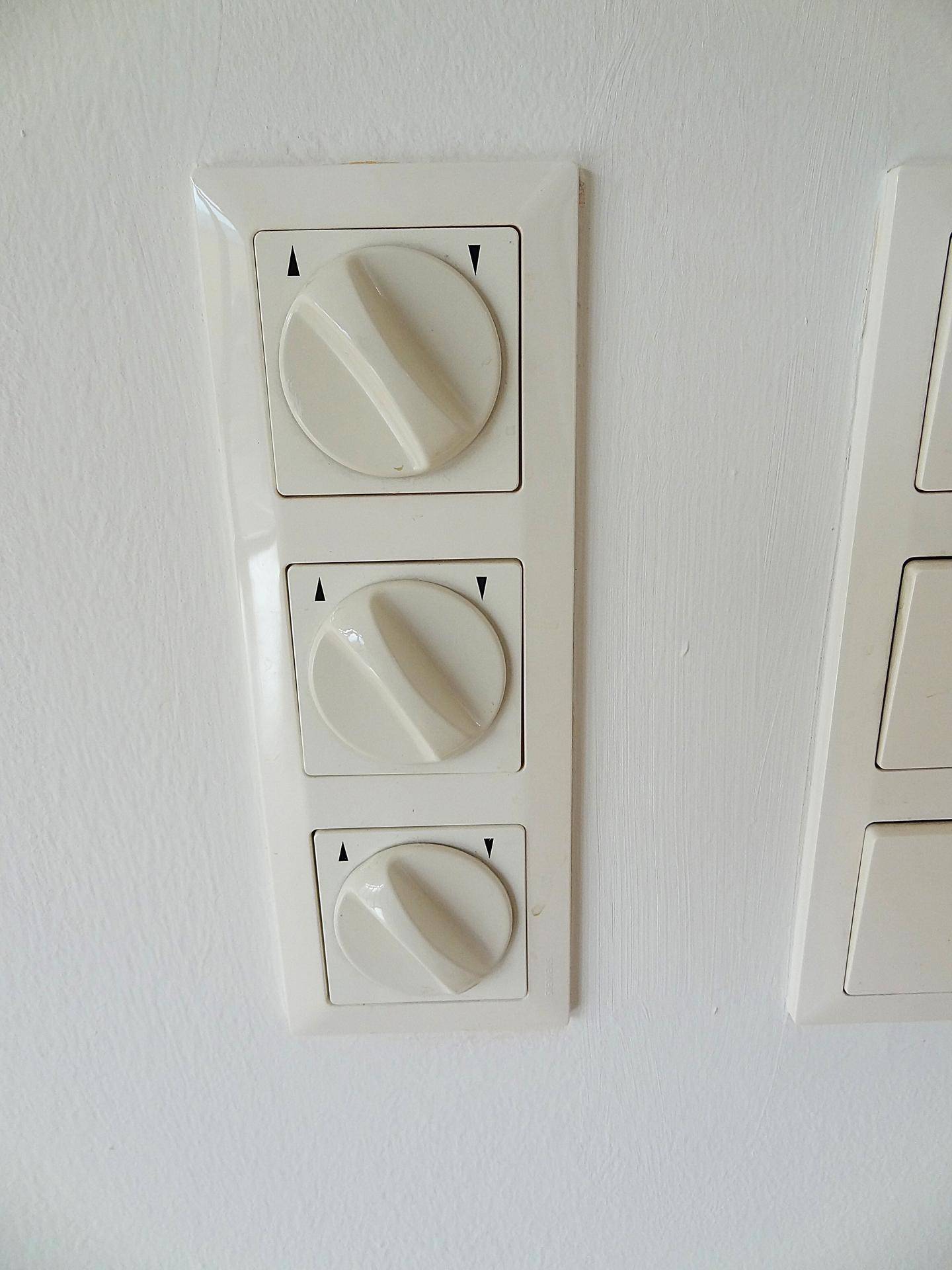 Detailaufnahme von drei Lichtschaltern mit Drehreglern an einer weißen Wand.