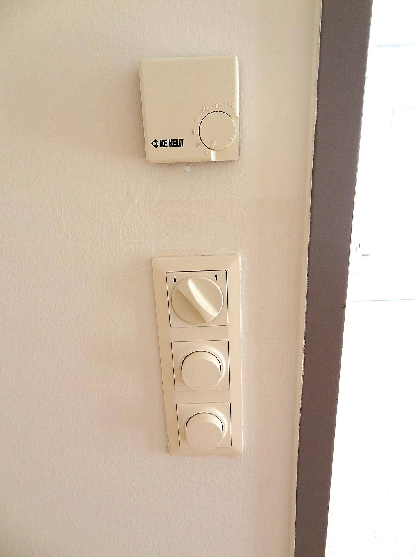 Detailaufnahme von Wandreglern und einem Thermostat an einer hellen Wand.