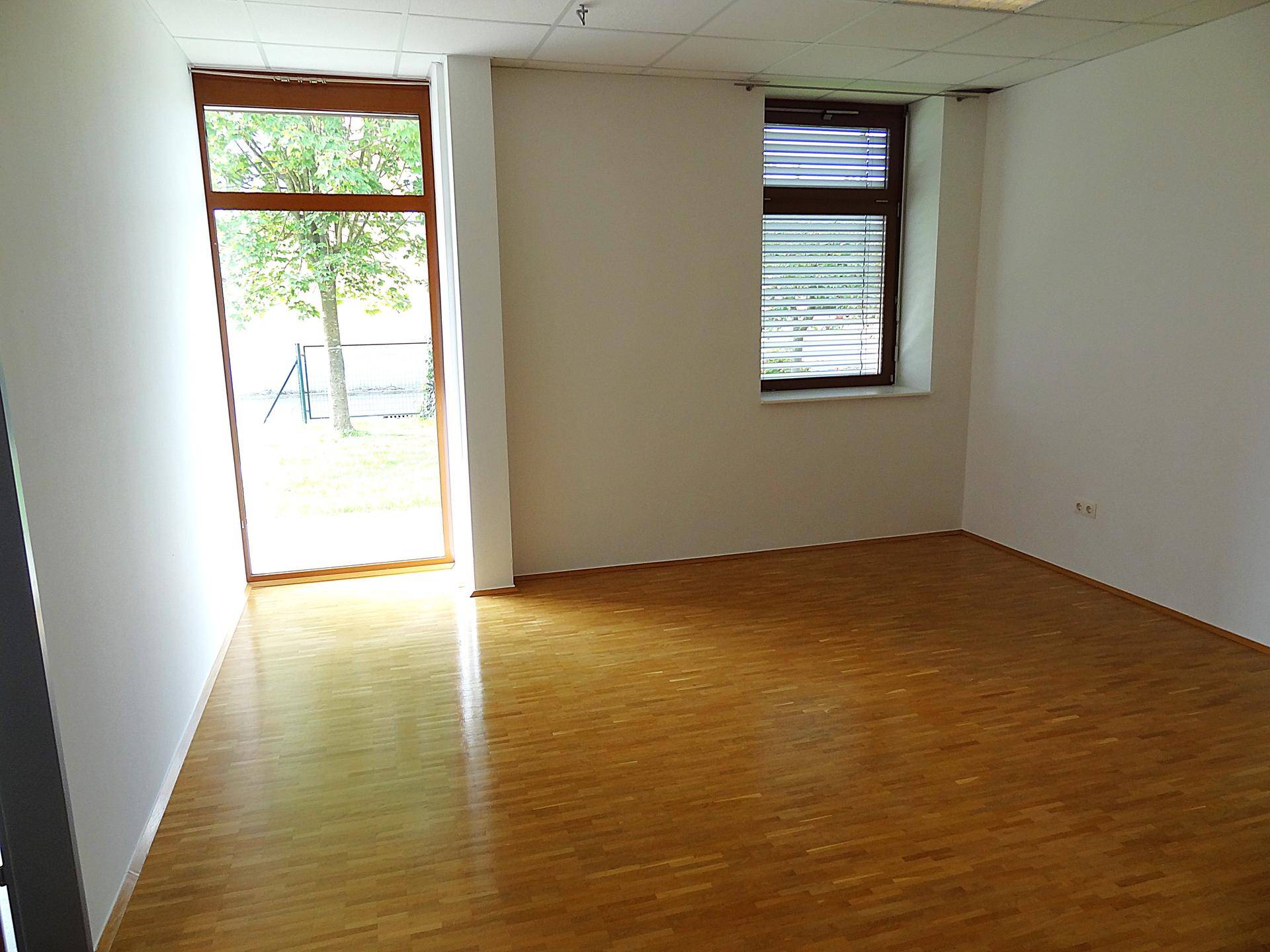 Heller Büroraum mit Holzboden, großen Fenstern und Blick ins Grüne.