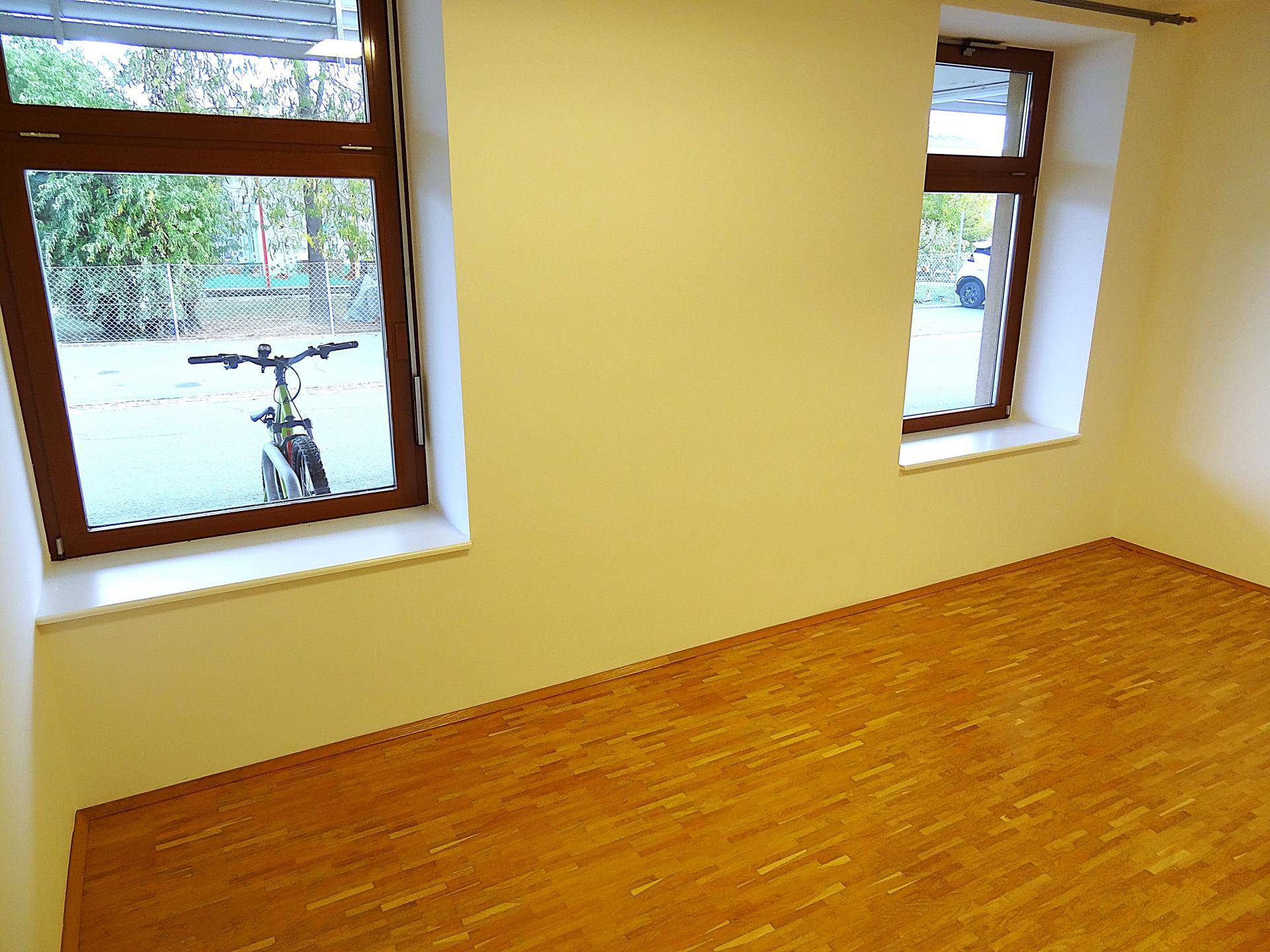 Büroraum mit Holzboden und zwei Fenstern, die einen Blick nach draußen bieten.
