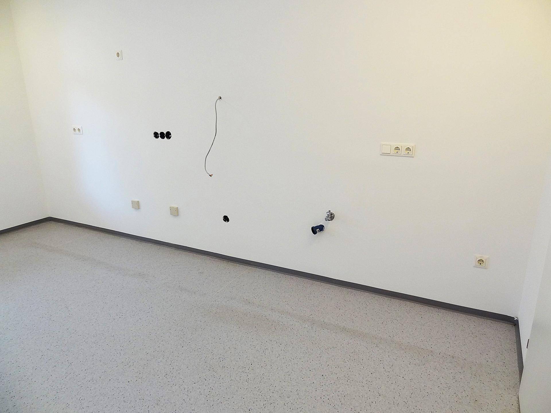 Detailansicht einer Wand mit Steckdosen, Kabeln und Anschlüssen in einem leeren Raum.