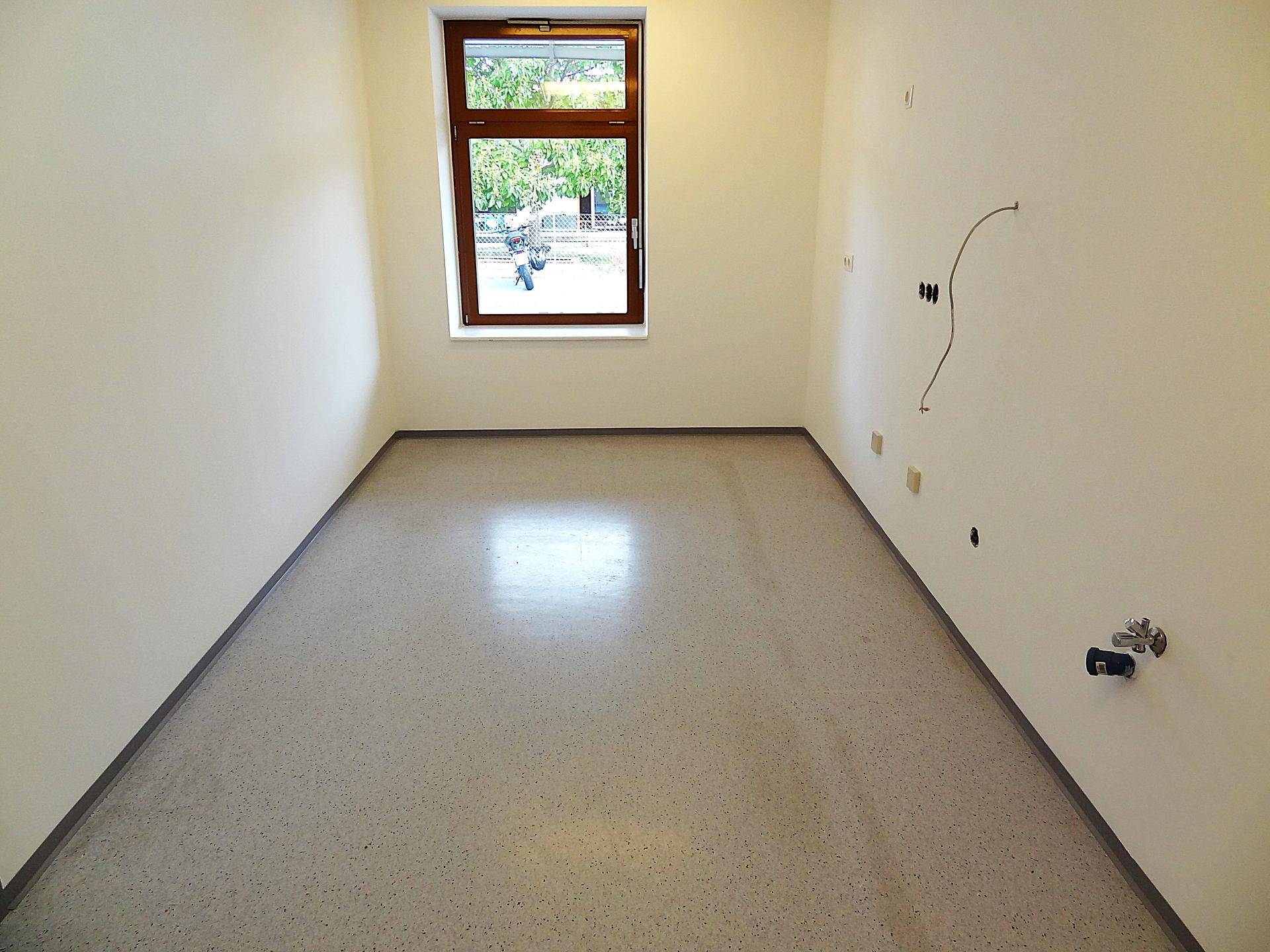 Heller Raum mit hellem Boden, Fenster und vorbereiteten Anschlüssen an der Wand.
