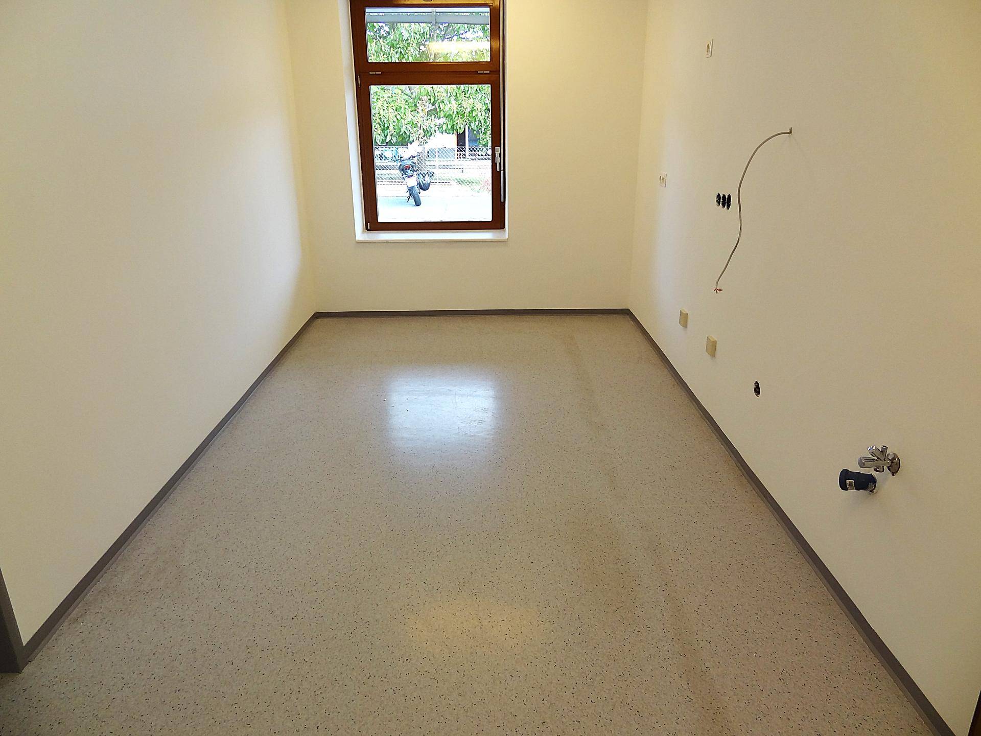 Heller, leerer Raum mit einem Fenster und vorbereiteten Anschlüssen an der Wand.