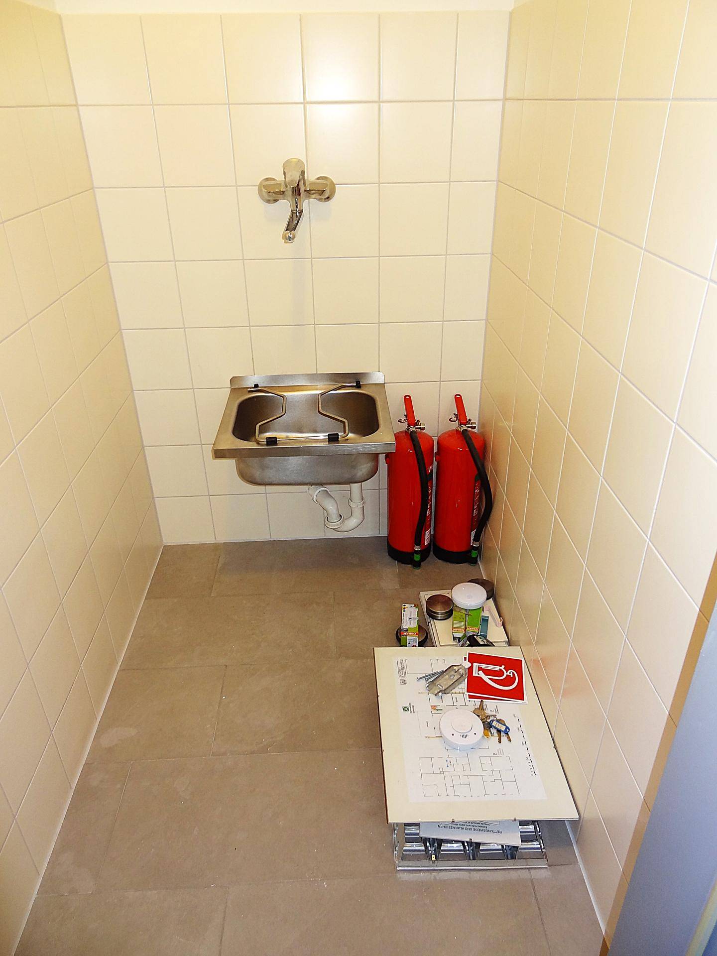 Nutzraum mit Edelstahlwaschbecken, Fliesenwänden und zwei Feuerlöschern.