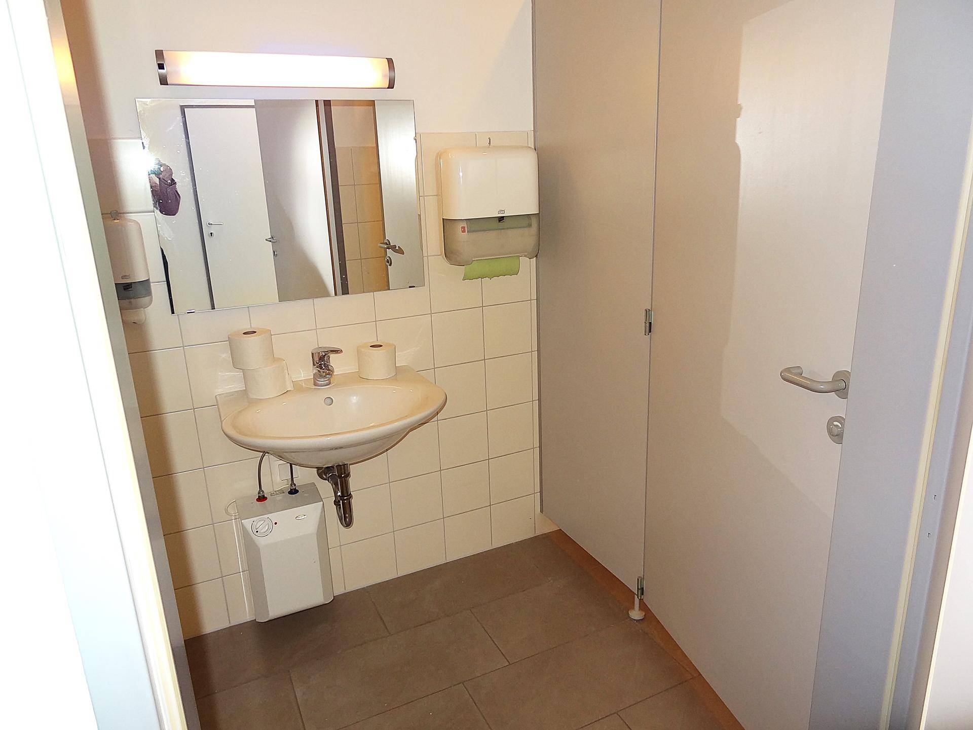 Badezimmer mit Waschbecken, Spiegel und weiß gefliesten Wänden, gut beleuchtet.