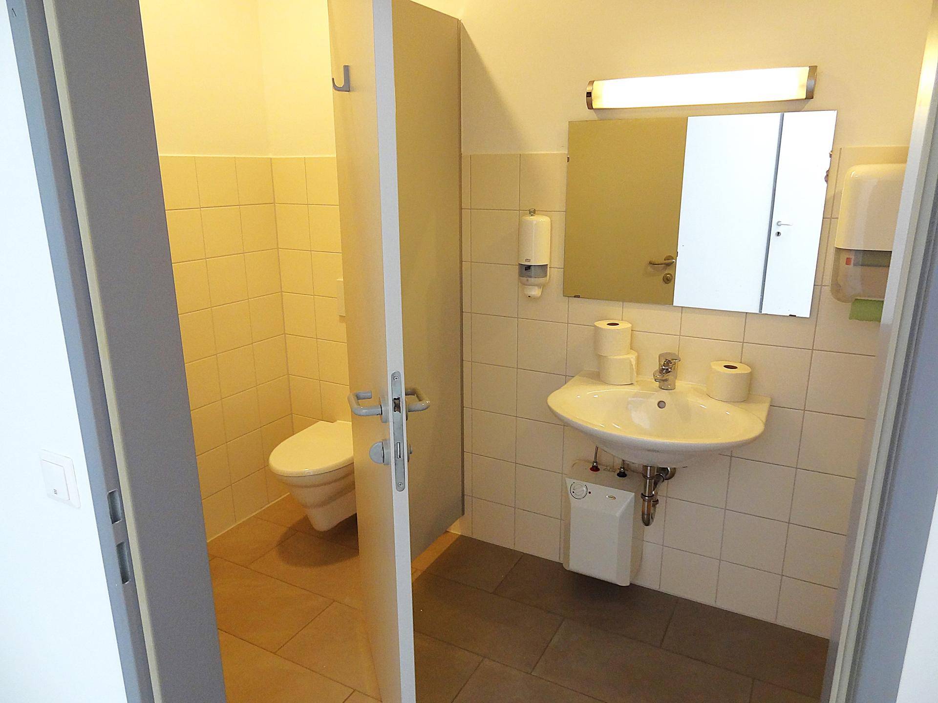 Badezimmer mit Waschbecken, Spiegel und Zugang zu einer separaten Toilette.