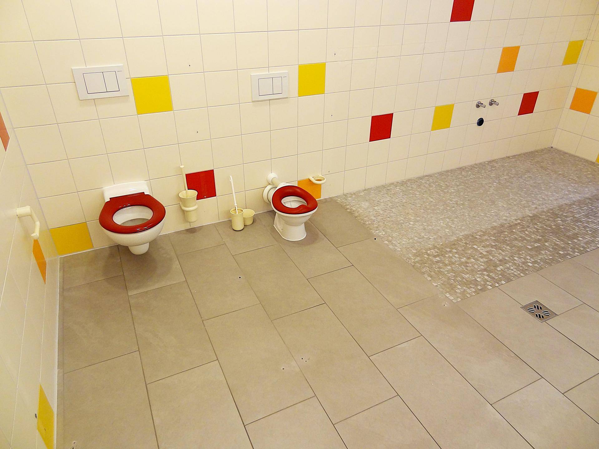 Buntes Kinderbadezimmer mit kleinen Toiletten und farbigen Fliesen an den Wänden.
