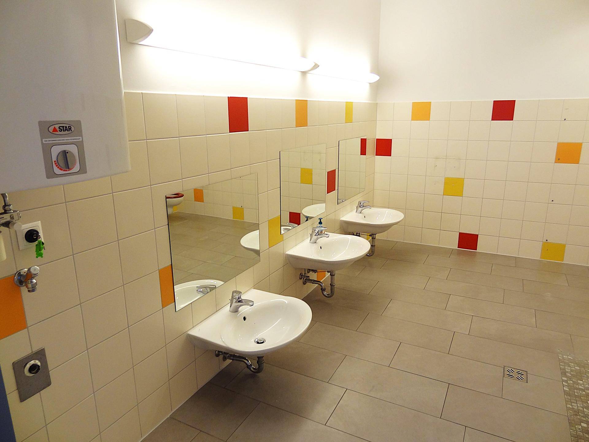 Buntes Kinderbadezimmer mit mehreren Waschbecken und Spiegeln, hell und freundlich.