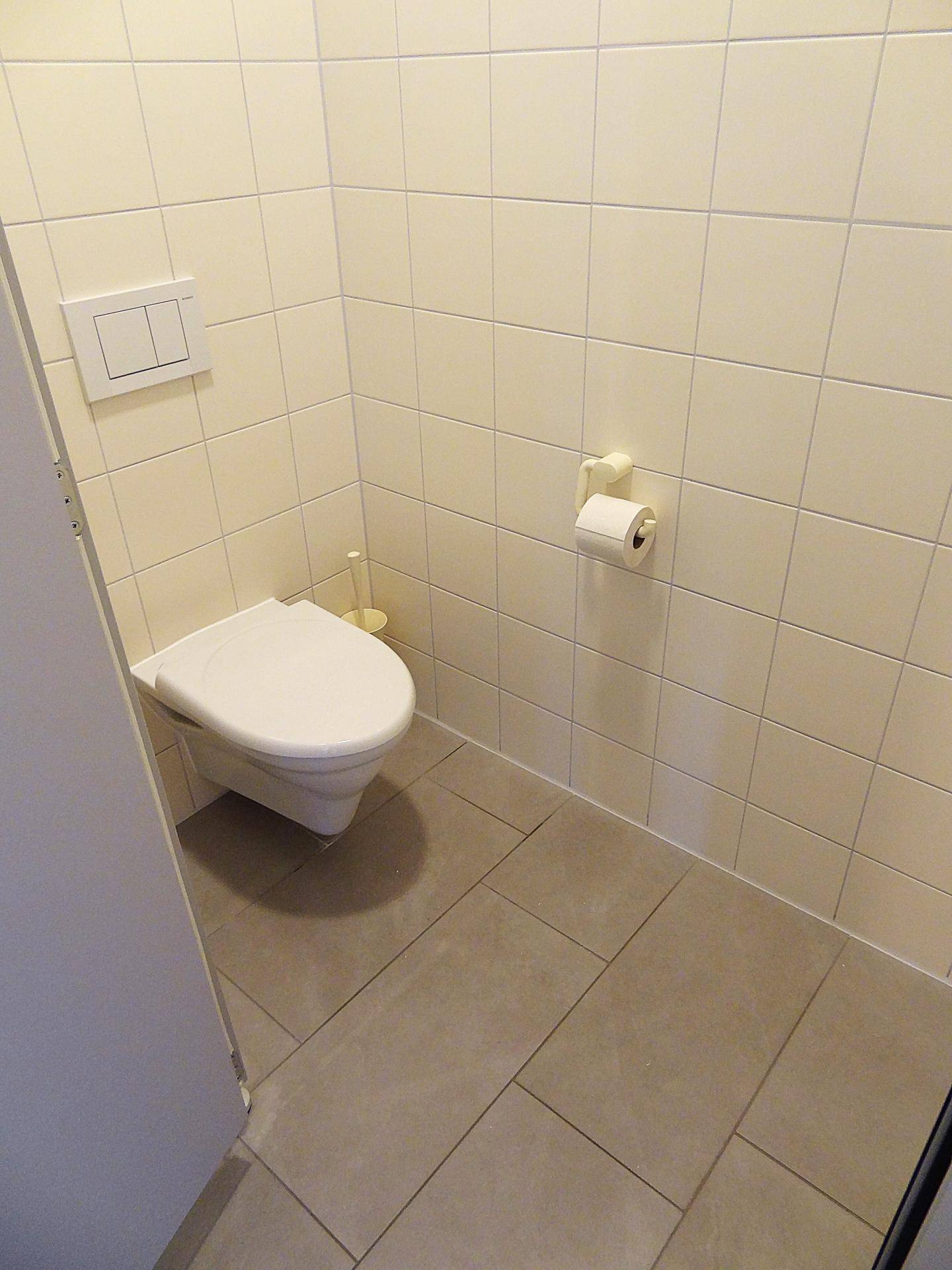 Separate Toilette mit Wand-WC und hellen Fliesen an Wänden und Boden.