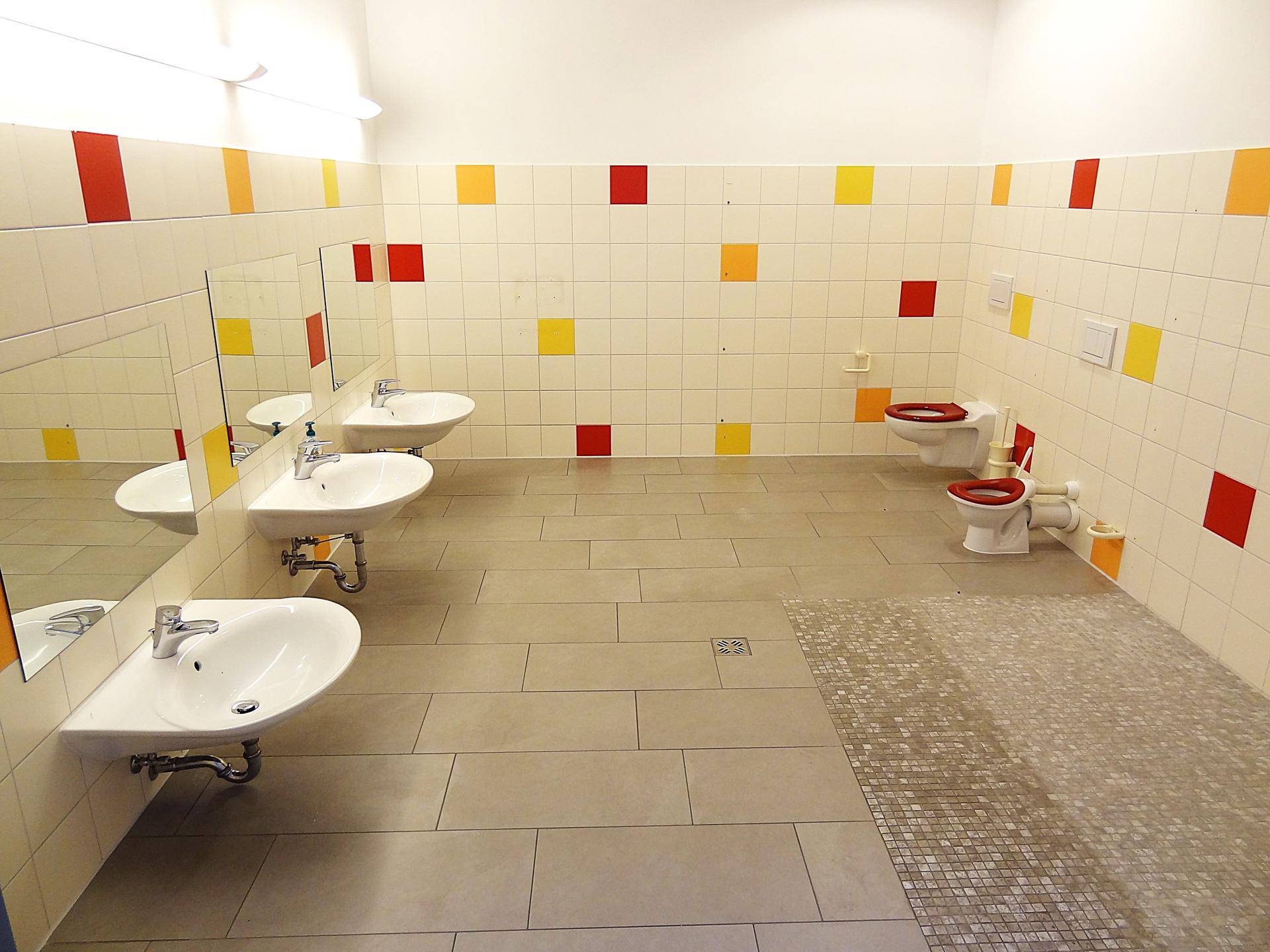 Buntes Kinderbadezimmer mit mehreren Waschbecken und kleinen Toiletten, farbenfroh gefliest.