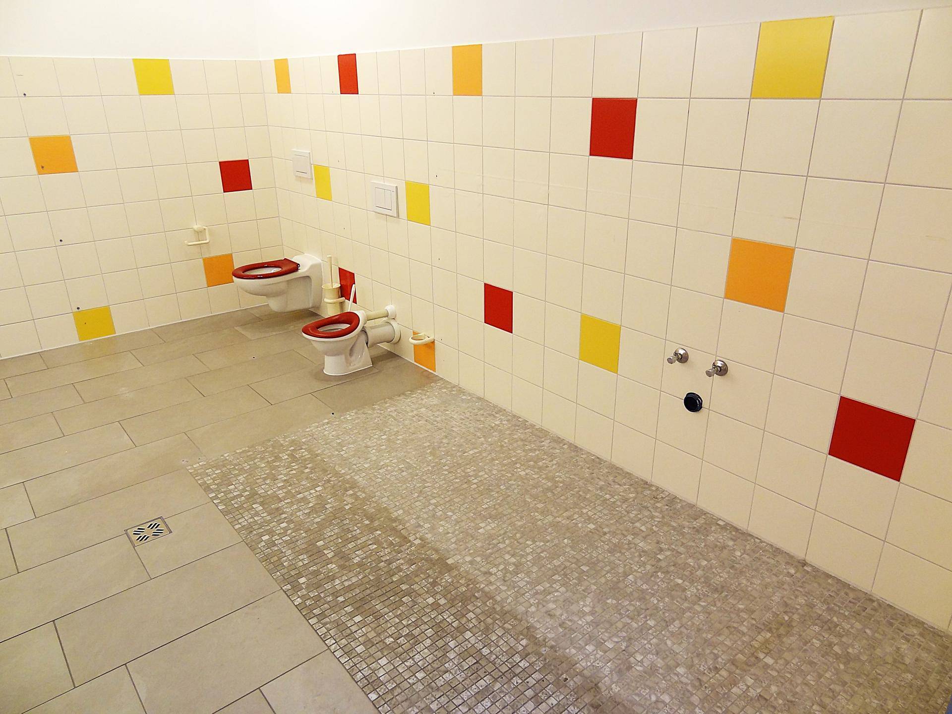 Buntes Kinderbadezimmer mit kleinen Toiletten und farbigen Fliesen an den Wänden.