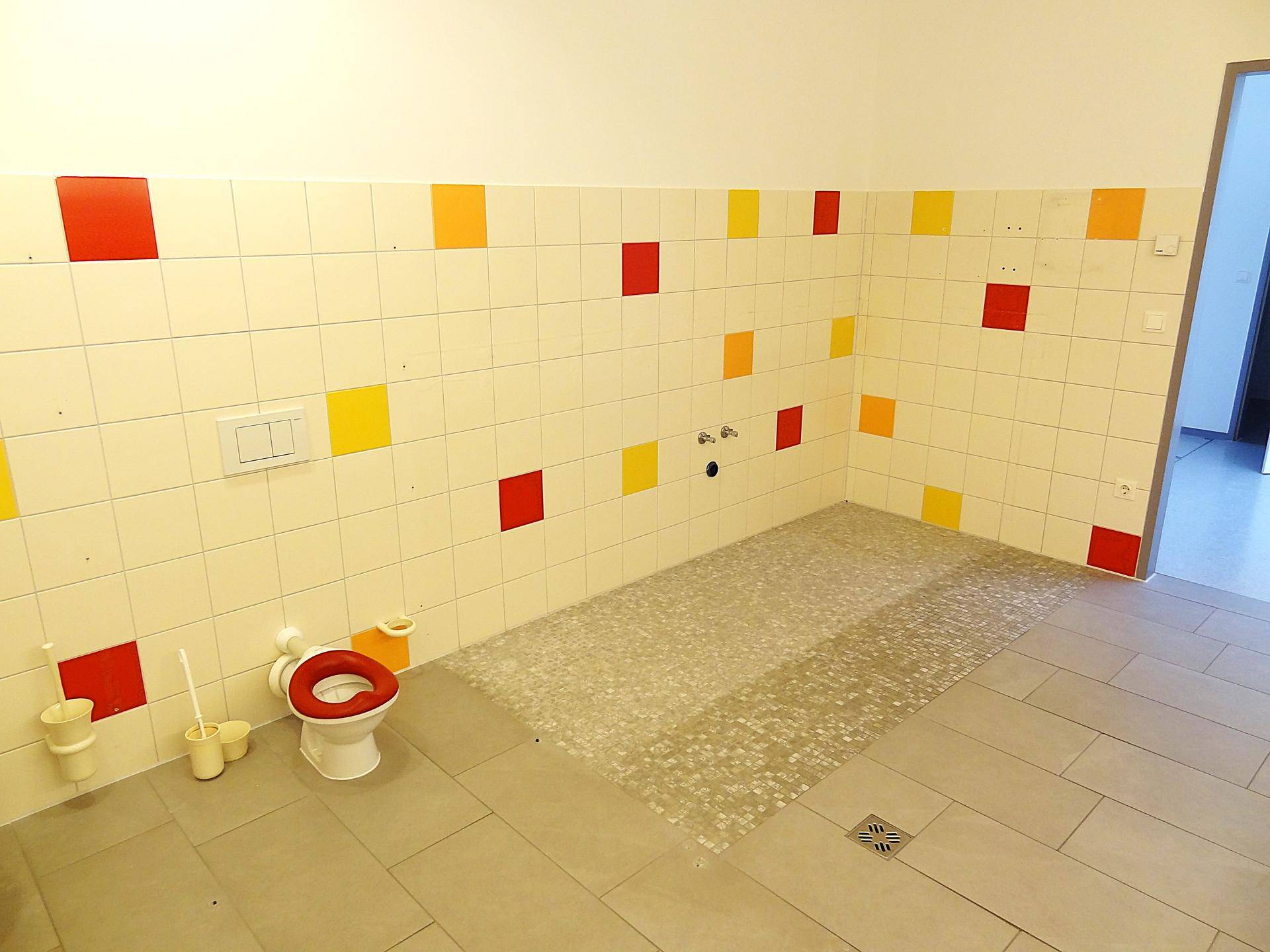 Buntes Kinderbadezimmer mit kleinen Toiletten und farbigen Fliesen an den Wänden.